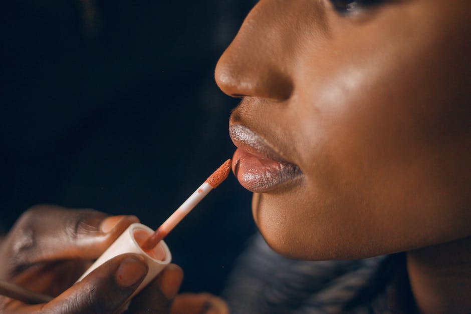 A detailed close-up of glossy lipstick being applied to a woman's lips, highlighting beauty and fashion trends