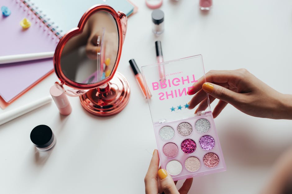 A vibrant eyeshadow palette with glittery colors held near a heart-shaped mirror