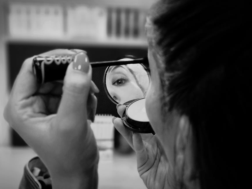 A woman applies makeup in monochrome, capturing a detailed eye reflection