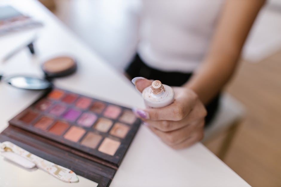 Close-up of a person holding foundation bottle with colorful makeup palette in focus