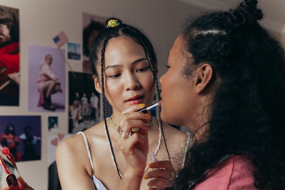 Two diverse women applying lipstick in a room adorned with posters, capturing a cozy and intimate moment
