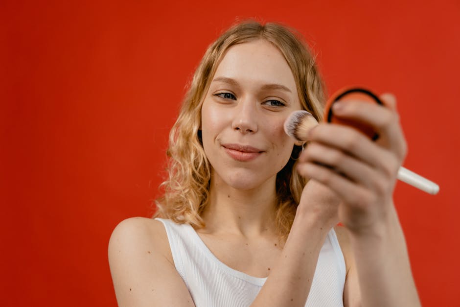 Woman applying makeup with a brush against a vibrant red backdrop, showcasing beauty and skincare concepts